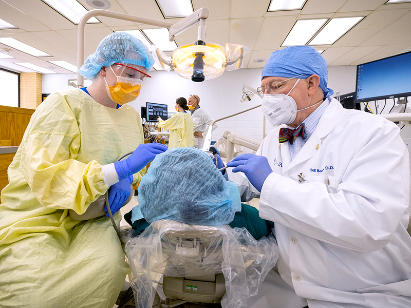 Third-year School of Dentistry student Elizabeth Karajman treats a patient with help from Dr. William Boteler.